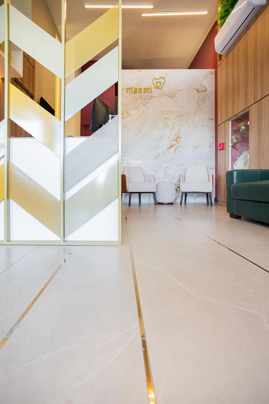 Recepção da Clínica Maesti com parede de mármore e o logo dourado